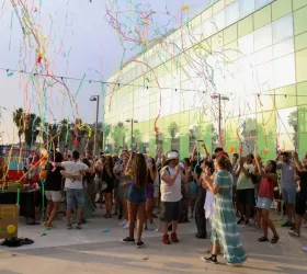 A crowd of people around a big building with colorful streamers